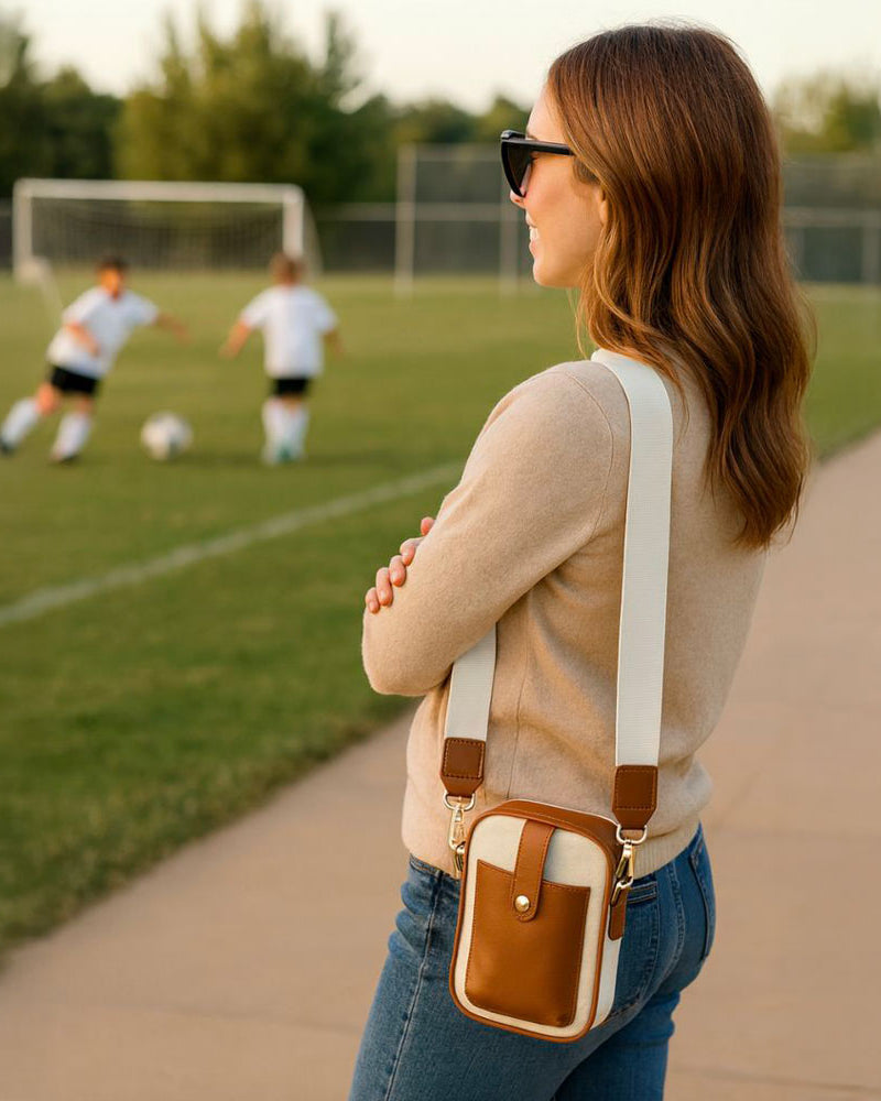 Woman with a canvas crossbody bag watching children play soccer on a field