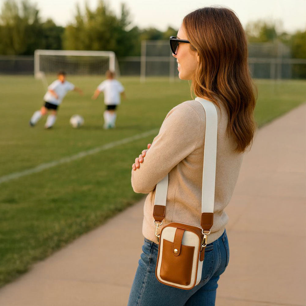 Woman with a canvas crossbody bag watching children play soccer on a field