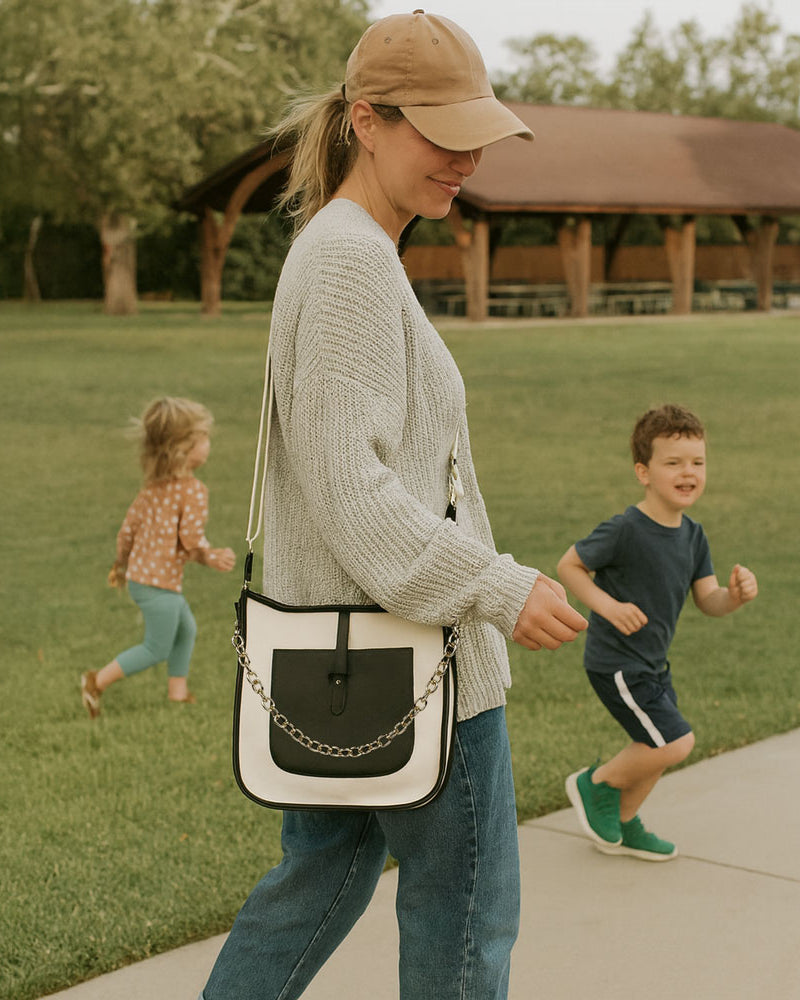 Woman walking with two children in a park, carrying a cream and black canvas handbag.