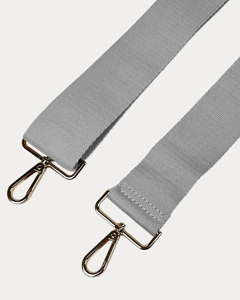 Gray bag strap with gold hardware on a light gray background