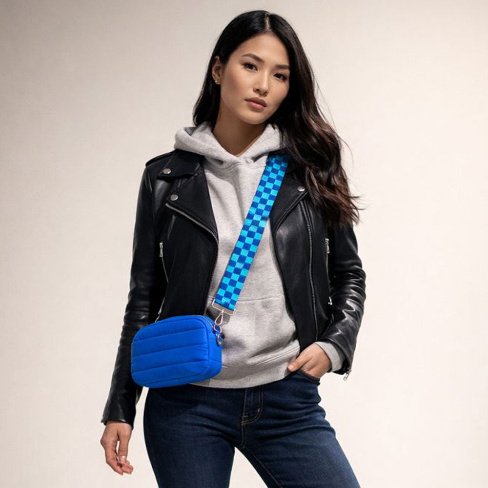 Woman wearing a black leather jacket, gray hoodie, and blue jeans with a blue bag featuring a Blue and Aqua checkerboard strap.