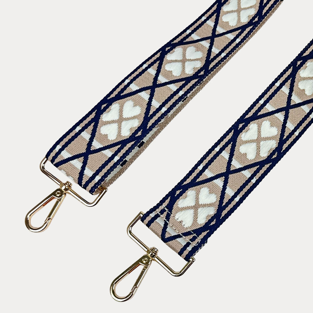 Tan, white, navy patterned bag strap with gold metal clasps on a light grey background.