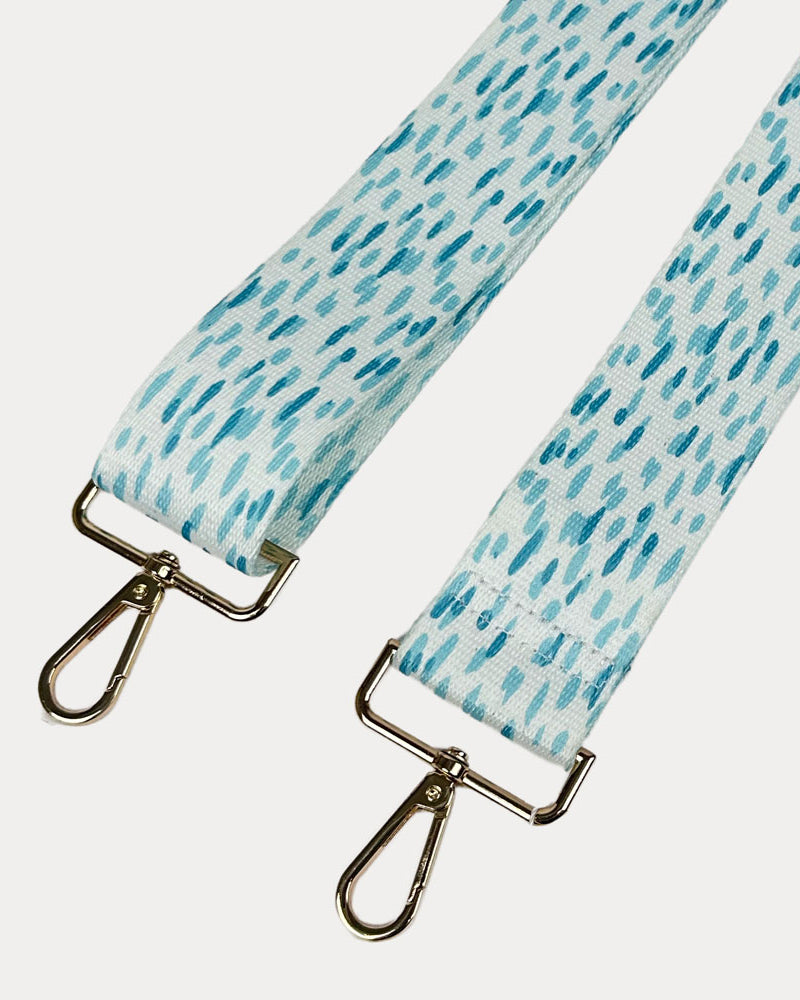 Aqua and white dot patterned bag strap with gold hardware on a light gray background