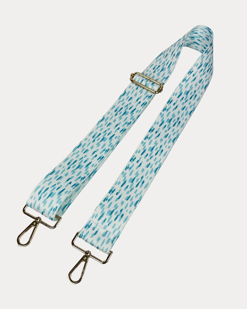 Aqua and white dot patterned bag strap with gold hardware on a light gray background