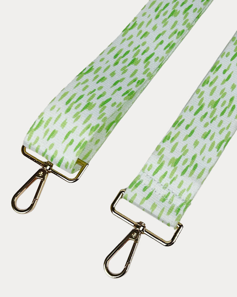 Green and white dot patterned bag strap with gold hardware on a light gray background