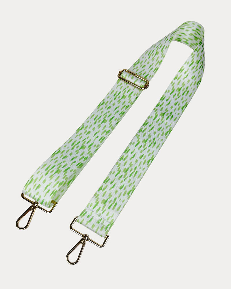 Green and white dot patterned bag strap with gold hardware on a light gray background