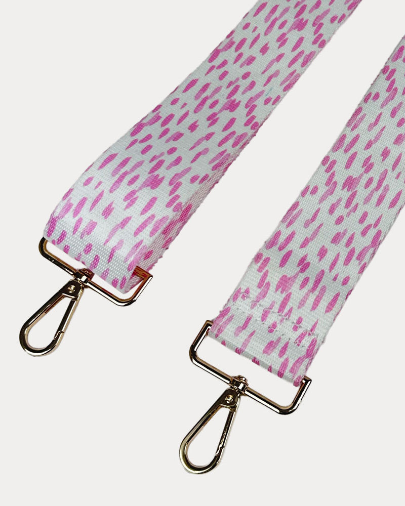 Pink and white dot patterned bag strap with gold hardware on a light gray background