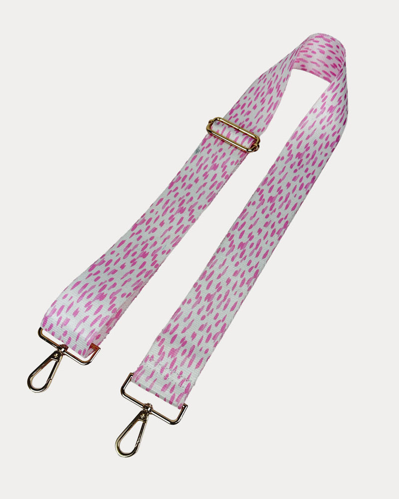 Pink and white dot patterned bag strap with gold hardware on a light gray background