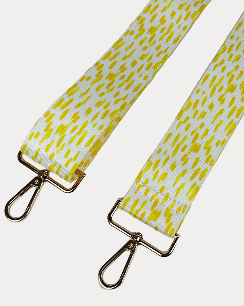 Yellow and white dot patterned bag strap with gold hardware on a light gray background