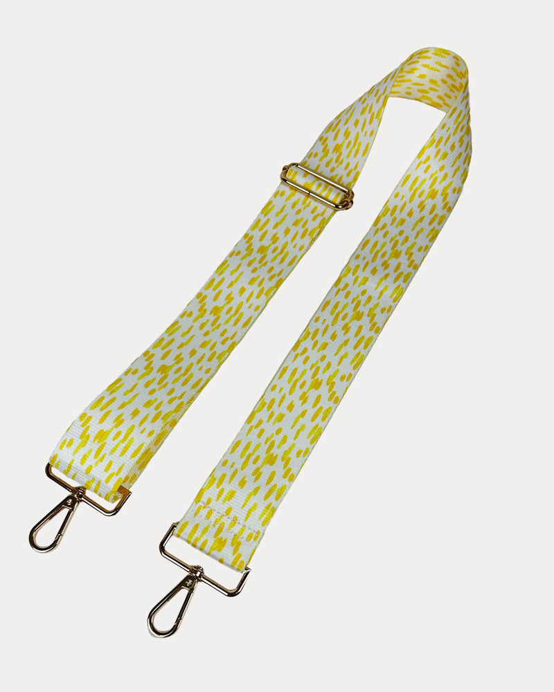 Yellow and white dot patterned bag strap with gold hardware on a light gray background
