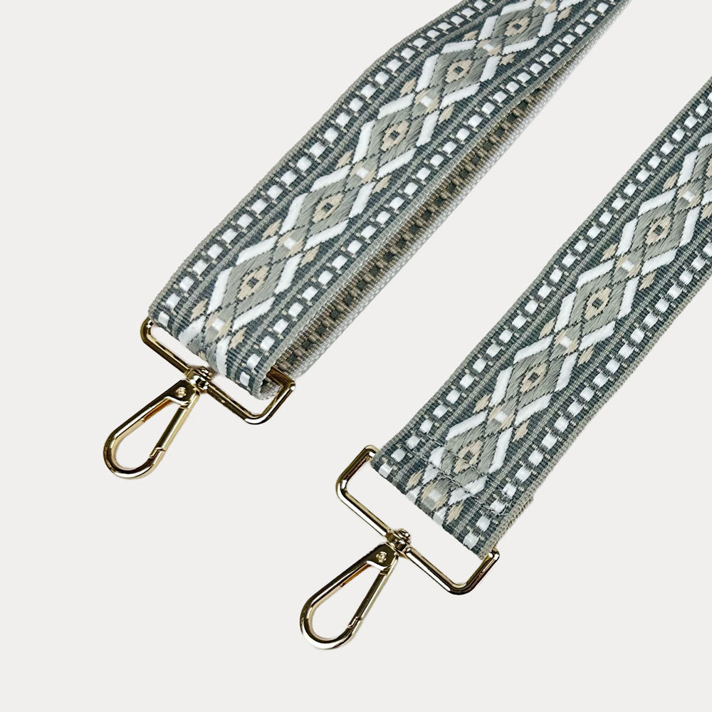 Grey, white, tan diamond patterned bag strap with gold metal clasps on a light gray background
