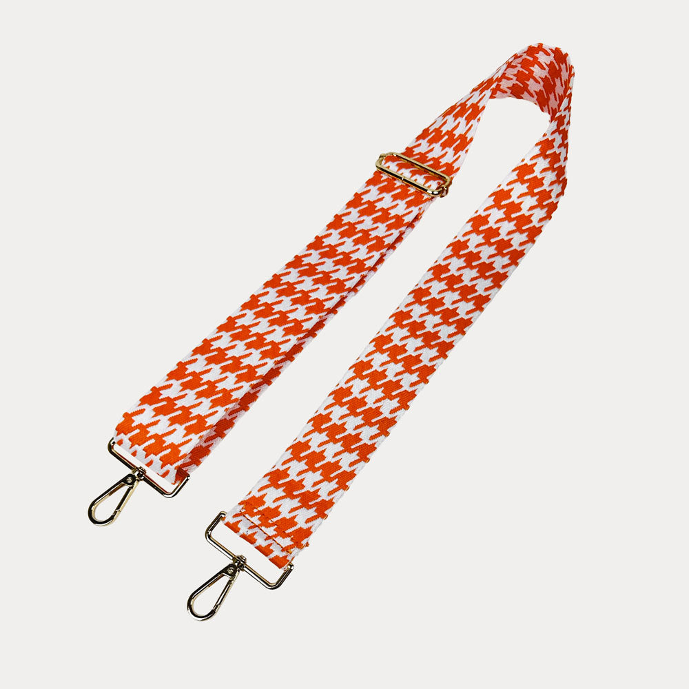 Orange and white houndstooth patterned strap with gold metal clasps on a light gray background