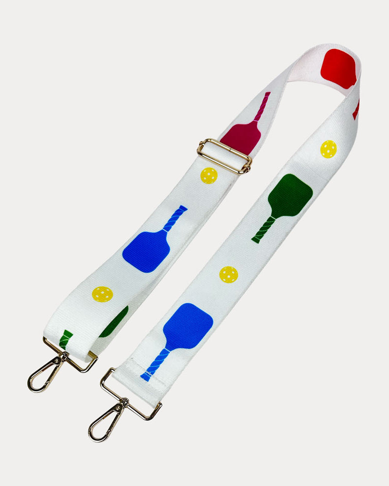 White ground with colorful pickleball paddles and white pickleball graphics with gold hardware bag strap