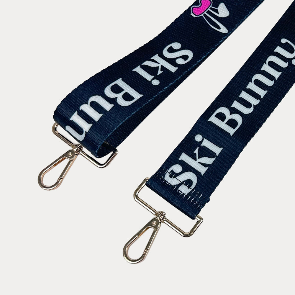 Black ground with Ski Bunny text in White and white bunny with pink accents printed bag strap with gold hardware