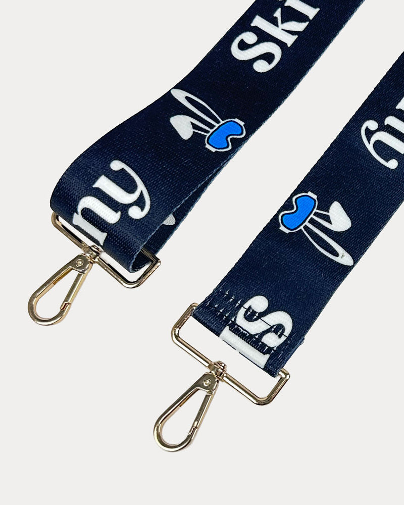 Black ground with Ski Bunny text in White and white bunny with blue accents printed bag strap with gold hardware