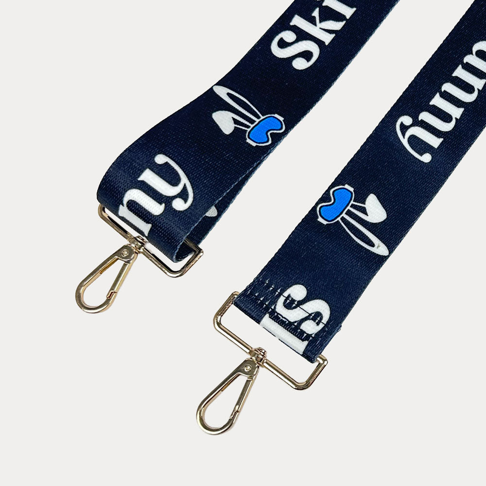 Black ground with Ski Bunny text in White and white bunny with blue accents printed bag strap with gold hardware