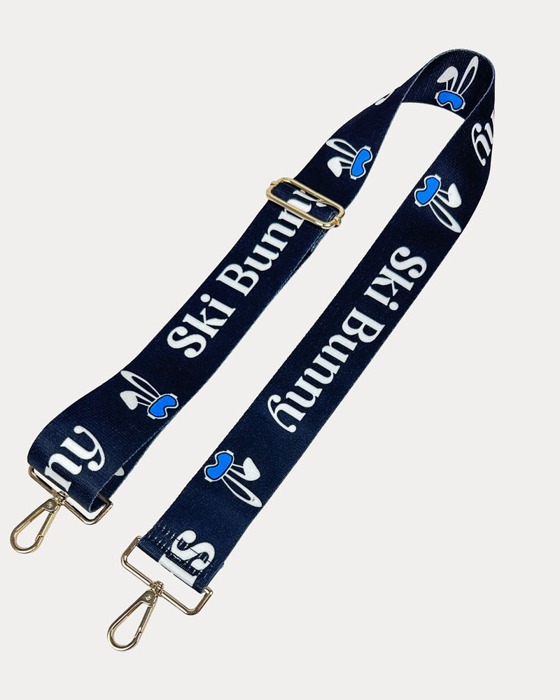 Black ground with Ski Bunny text in White and white bunny with blue accents printed bag strap with gold hardware