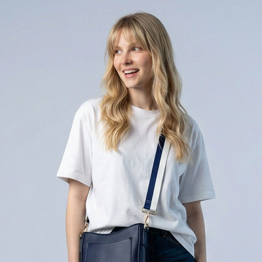 Woman wearing a white t-shirt with a navy and white stripe bag strap with a navy handbag against a light gray background