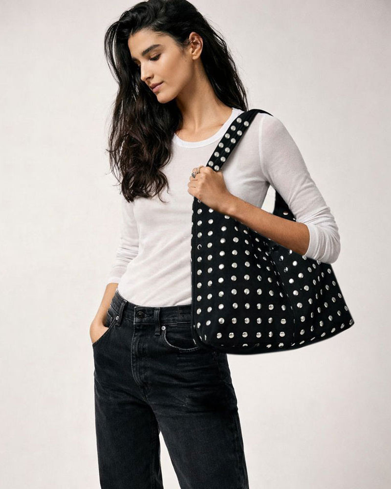Woman holding a black studded slouchy shoulder bag against a white background