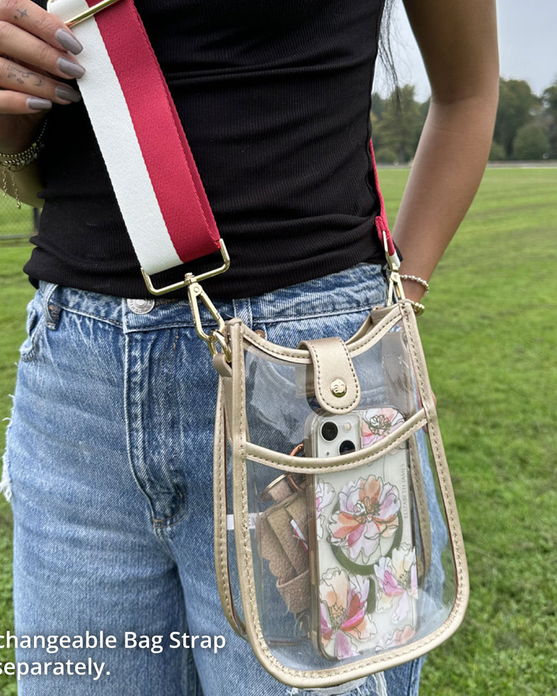 Person holding a transparent crossbody bag with a floral phone case in a grassy field.