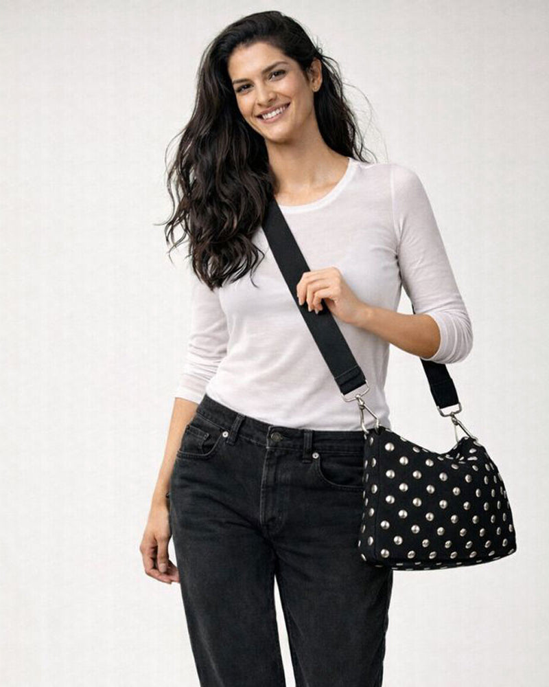 Woman wearing a black silver studded crossbody handbag against a white background
