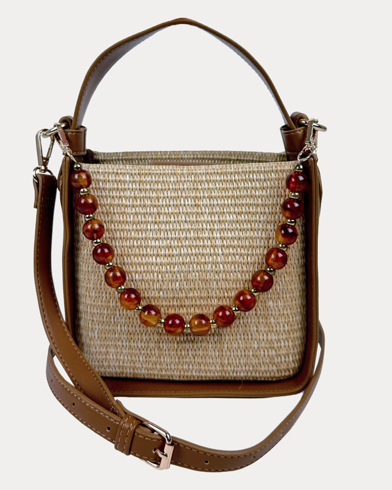 Raffia handbag with Camel Vegan Leather Details and a beaded strap on a light gray background
