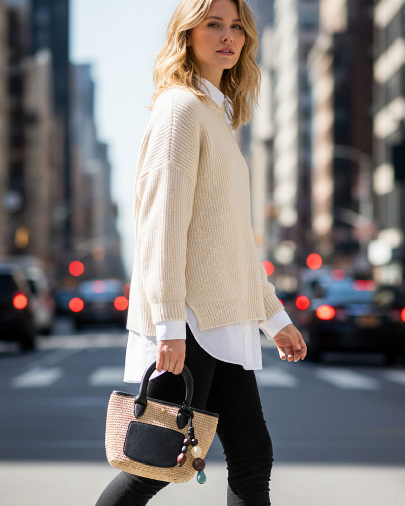 Woman walking on a city street holding a raffia tote with vegan black leather details and a beaded bag charm.