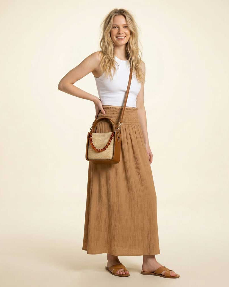 Woman wearing a Raffia handbag, wearing a white top and brown skirt on a beige background