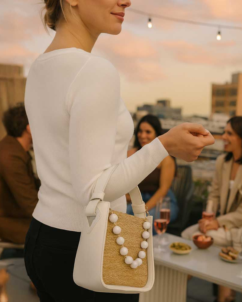 Woman holding a white handbag with a raffia design at an outdoor event.