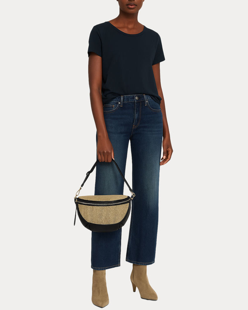 Woman holding a raffia sling bag in her hand down by her side.