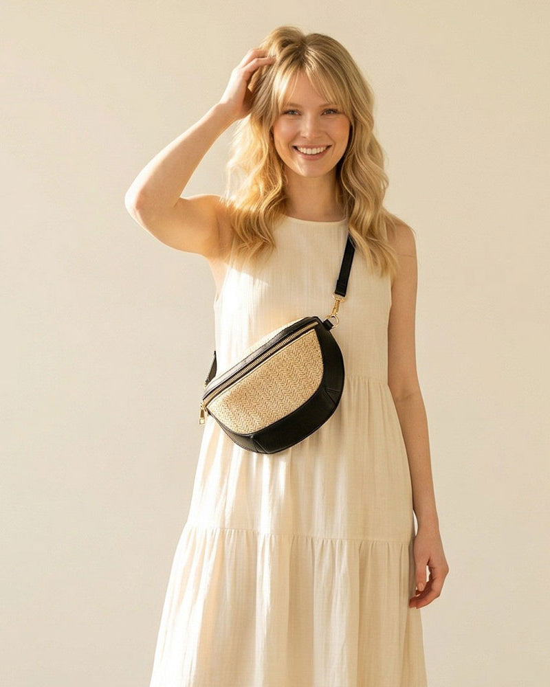 Woman in a beige dress holding a black and raffia sling bag against a plain background