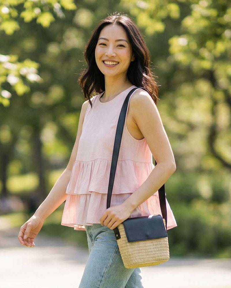 Woman in a pink sleeveless top and jeans wearing a raffia handbag on her shoulder.