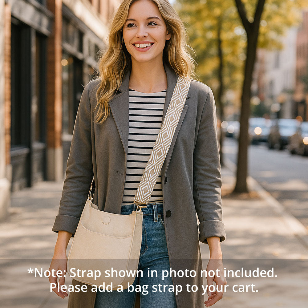 Woman walking on a city street wearing a gray coat with a cream messenger bag with a bag strap over her shoulder.