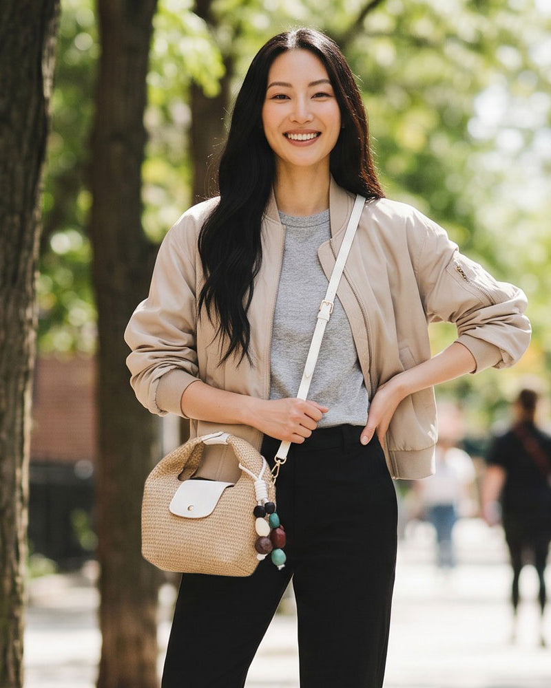 Woman standing outdoors with a raffia handbag, trees in the background