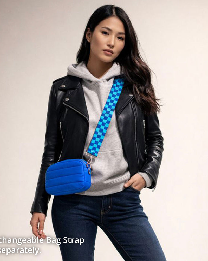 Woman wearing a black leather jacket, gray hoodie, and blue jeans with a blue crossbody bag on a beige background