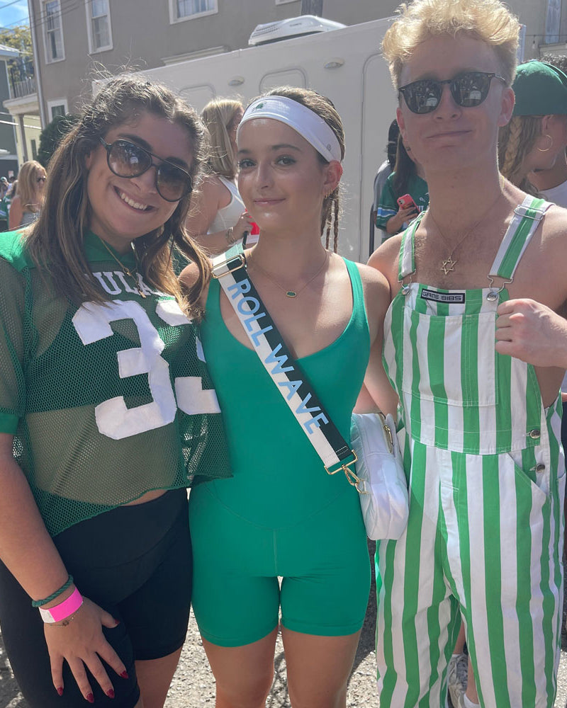 Group of friends outside at a football tailgate. One is wearing the green & white striped game day bag strap
