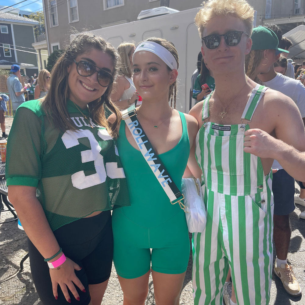 Group of friends outside at a football tailgate.  One is wearing the green & white striped game day bag strap