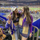 2 woman posing in a football stadium.  One is wearing the white and purple game day striped bag strap