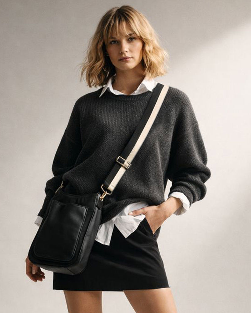 Woman wearing a black sweater and holding a black bag against a neutral background