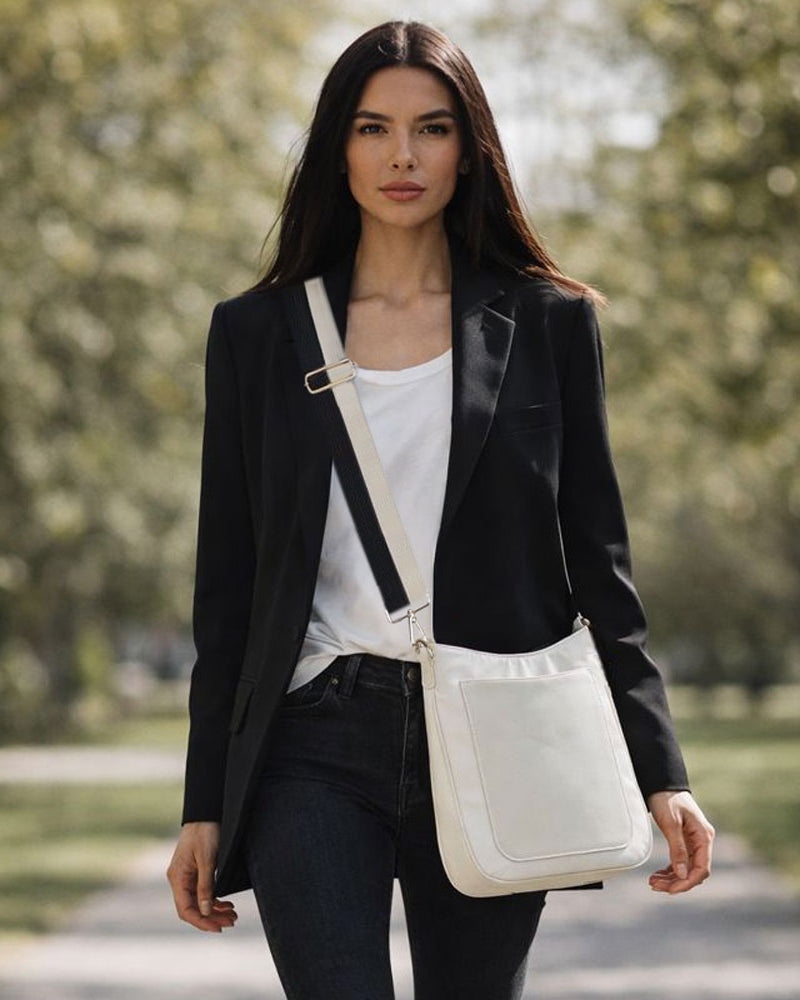 Woman in a black blazer and white shirt carrying a cream crossbody bag in a park.