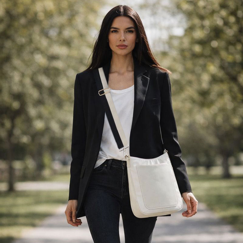Woman in a black blazer and white shirt carrying a cream crossbody bag in a park.