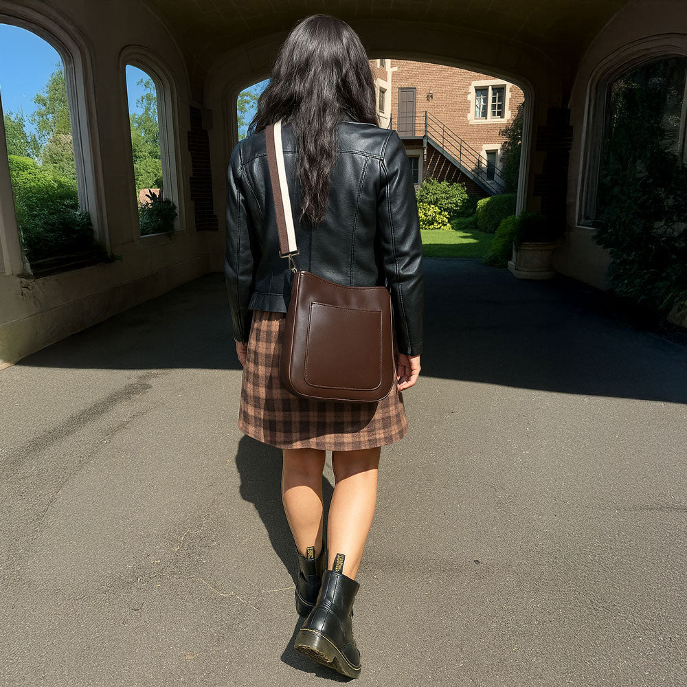 Person wearing a black leather jacket, plaid skirt, and brown boots walking outdoors.
