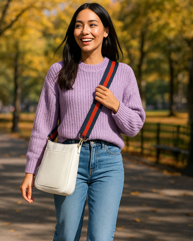 Woman walking in the park wearing the cream crossbody bag and navy-red striped bag strap