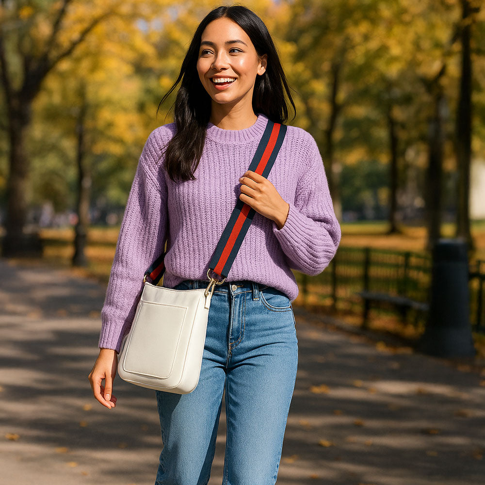 Woman walking in the park wearing the cream crossbody bag and navy-red striped bag strap