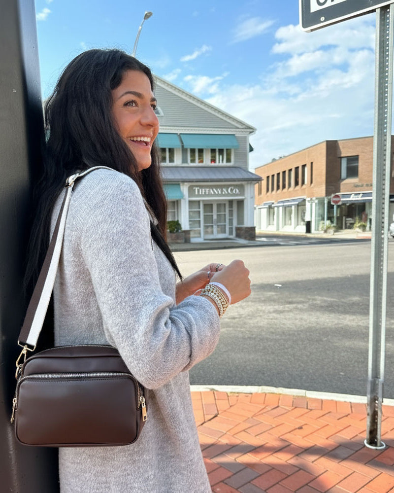 Woman with a brown handbag standing on a sidewalk with a street and buildings in the background
