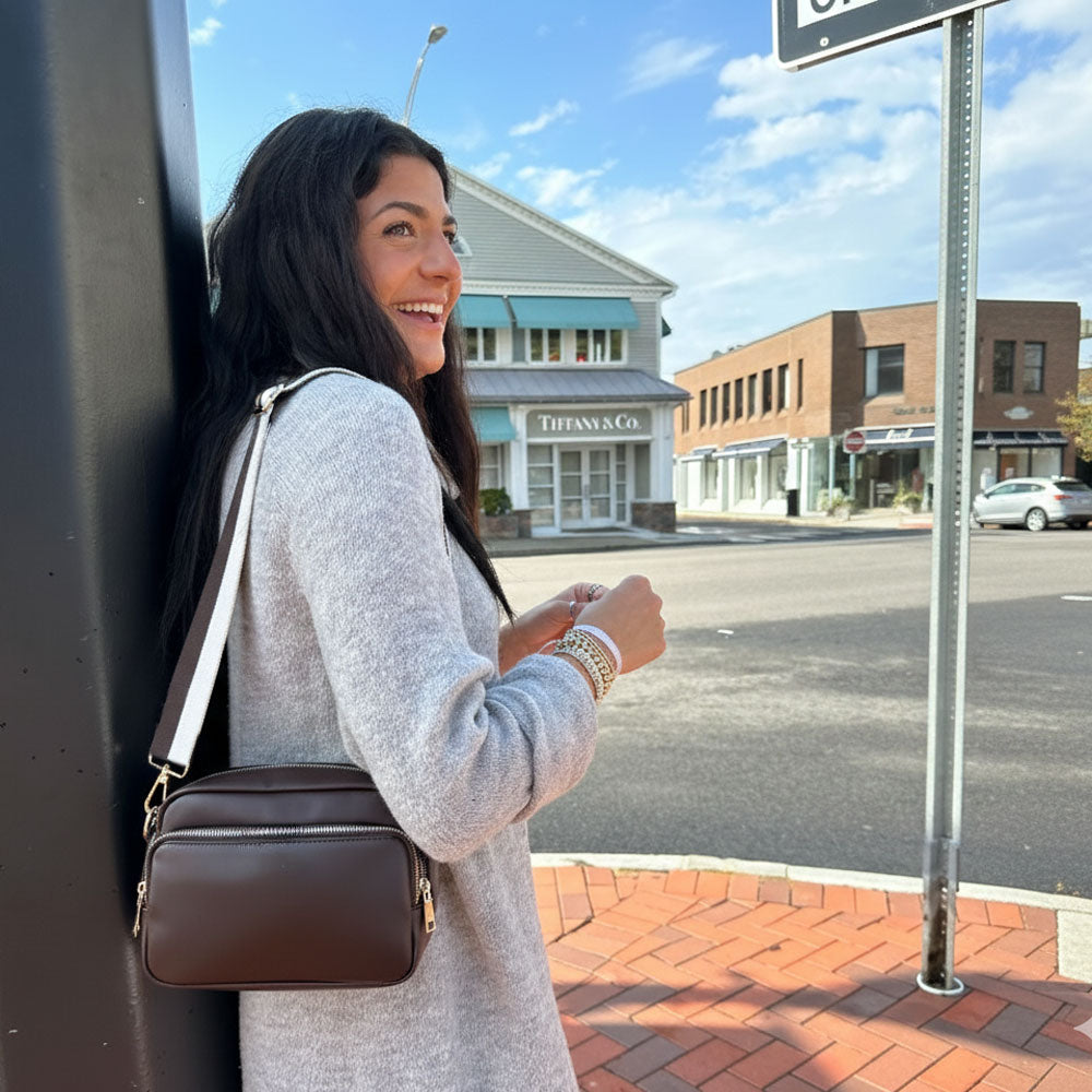 Woman with a brown handbag standing on a sidewalk with a street and buildings in the background