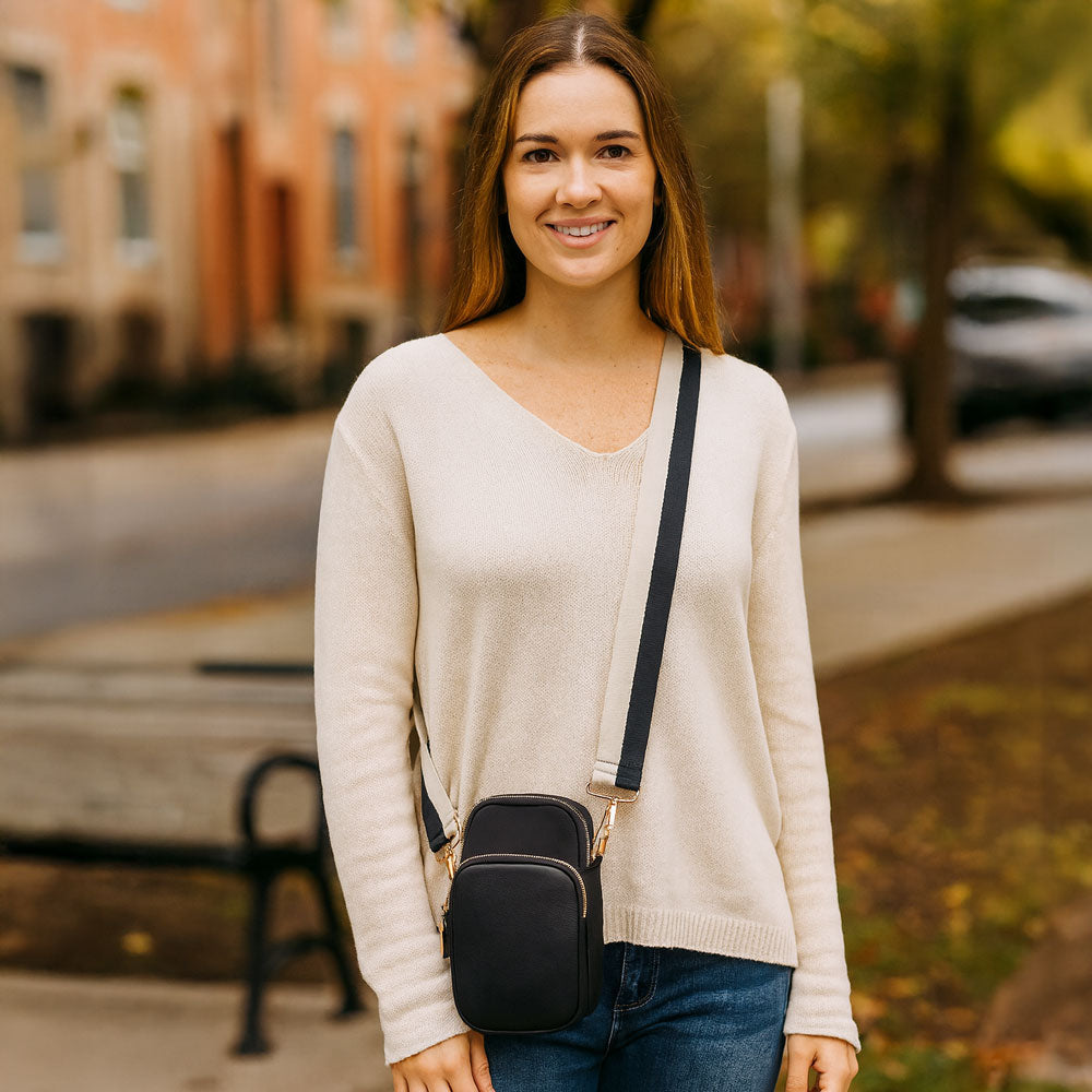 Woman in the park, wearing a black crossbody bag with a striped bag strap.