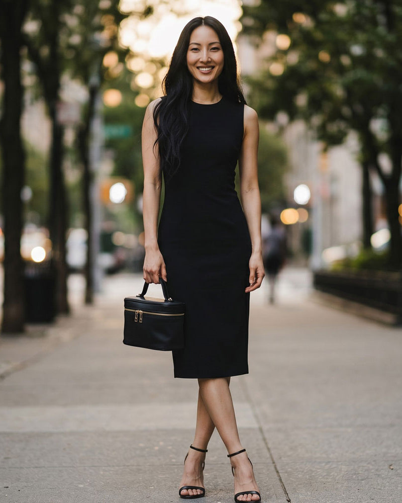 Woman in a black dress holding a black handbag on a city street.