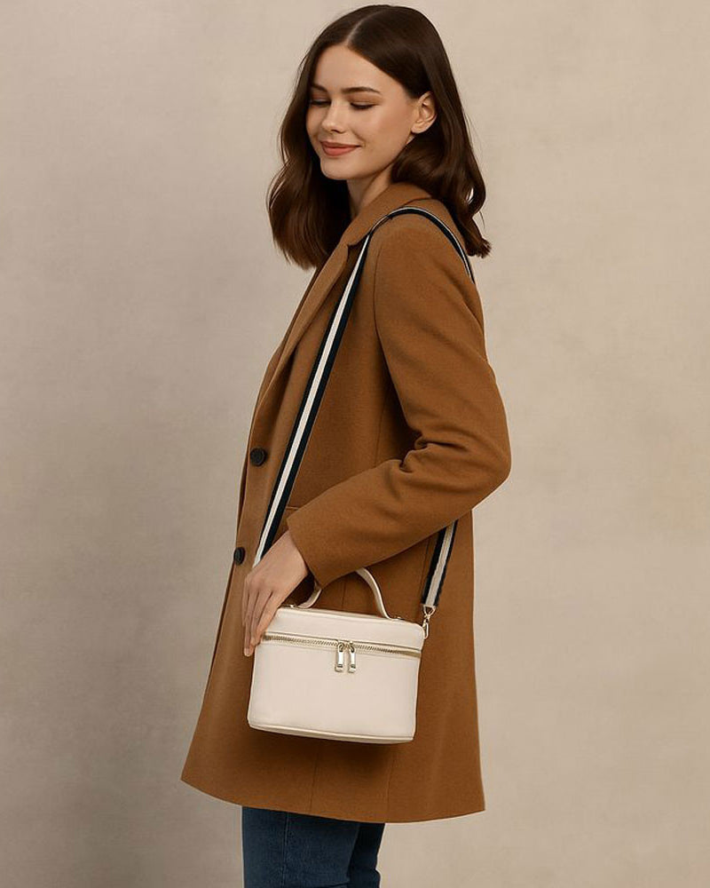 Woman in a brown coat holding a cream handbag against a beige background
