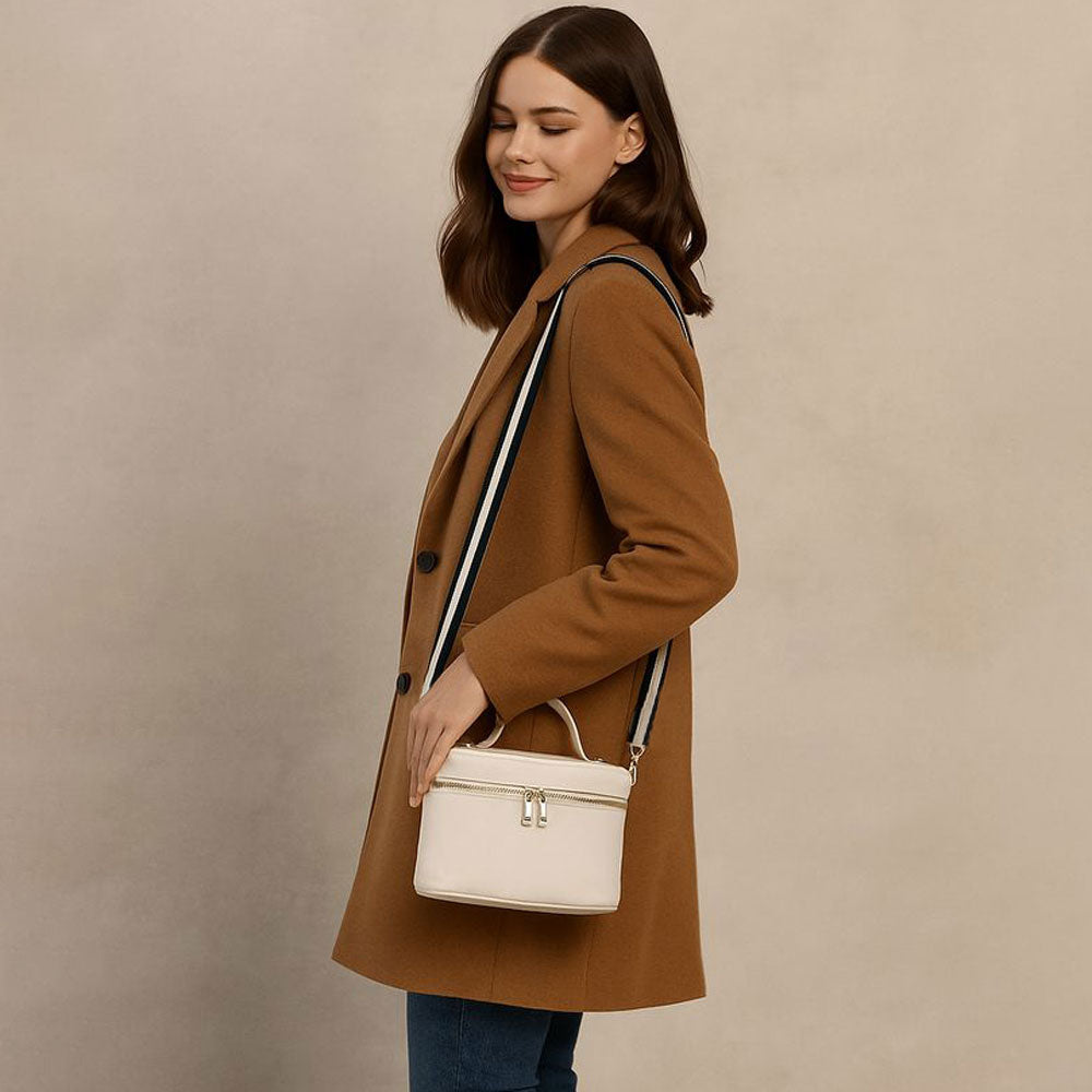 Woman in a brown coat holding a cream handbag against a beige background
